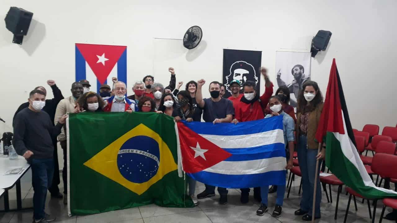 Participantes do evento segurando bandeiras do Brasil, Cuba e da Palestina. Créditos Coletivo José Martí de Solidariedade à Cuba e aos Povos em Luta